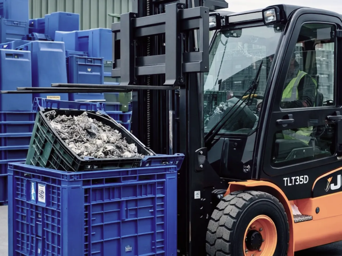 Forklift lifting a crate of plastic waste beside stacked blue containers