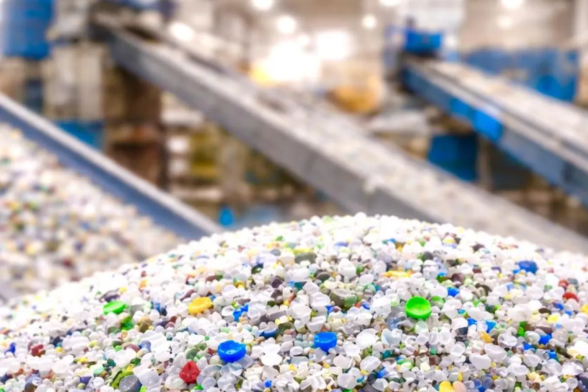 A heap of mixed plastic regrind beside conveyor belts in a recycling plant