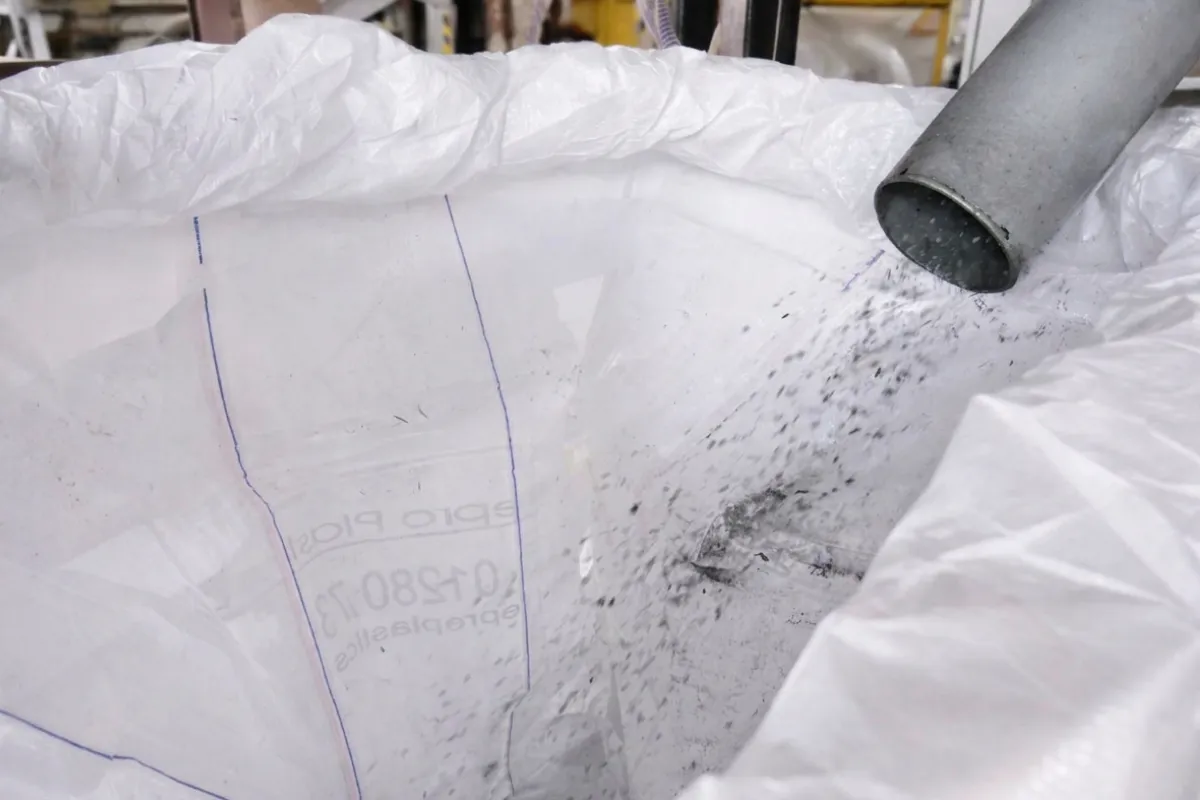 Recycled plastic granulate pouring from a pipe into a bulk bag